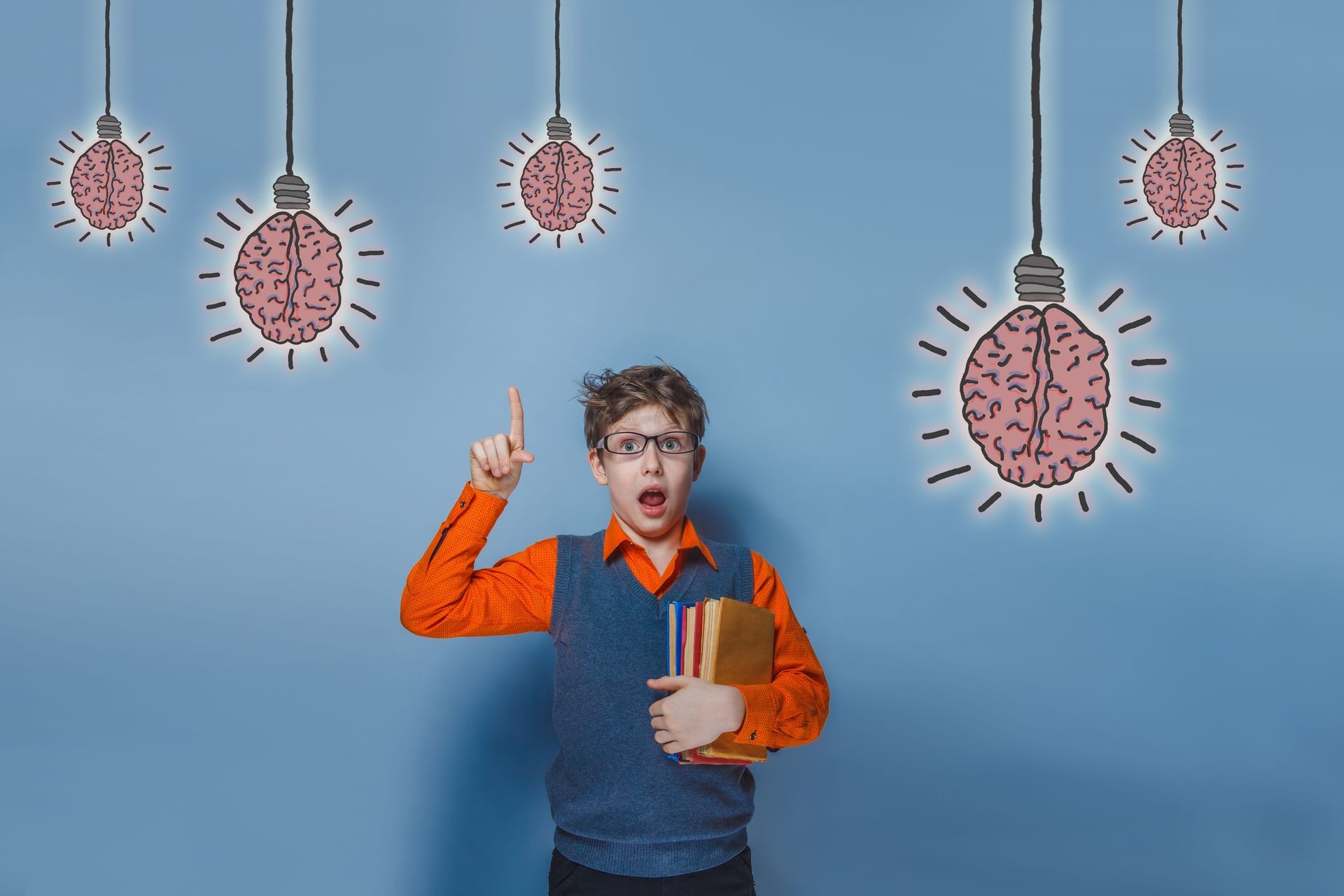 adolescent boy in glasses holding a book and opened his mouth, points a finger at the brain bulb creative idea